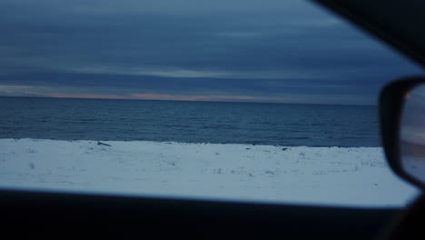 icelandic arctic highway winding through snowy plains alongside of open ocean frigid waters under twilight skies in winter