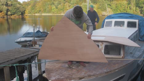 two men repairing a wooden boat on a lake
