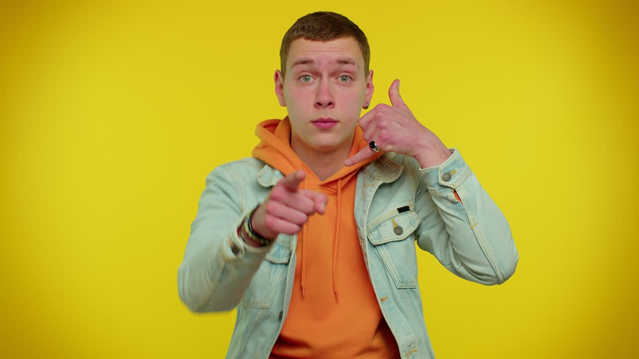 젠임 재을 입은 십대 남자가 카메라를 바라보며 전화 제스처를 하고 있습니다. "이봐요, 전화해 주세요".