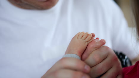 happy parents kissing their newborn baby. father's hand holding tiny infant's bare feet and kissing them. close up.