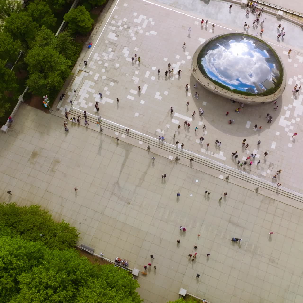 Chicago Bean in the middle of the square surrounded by greenery. Sky and skyscrapers reflecting in the Cloud Gate. Aerial view