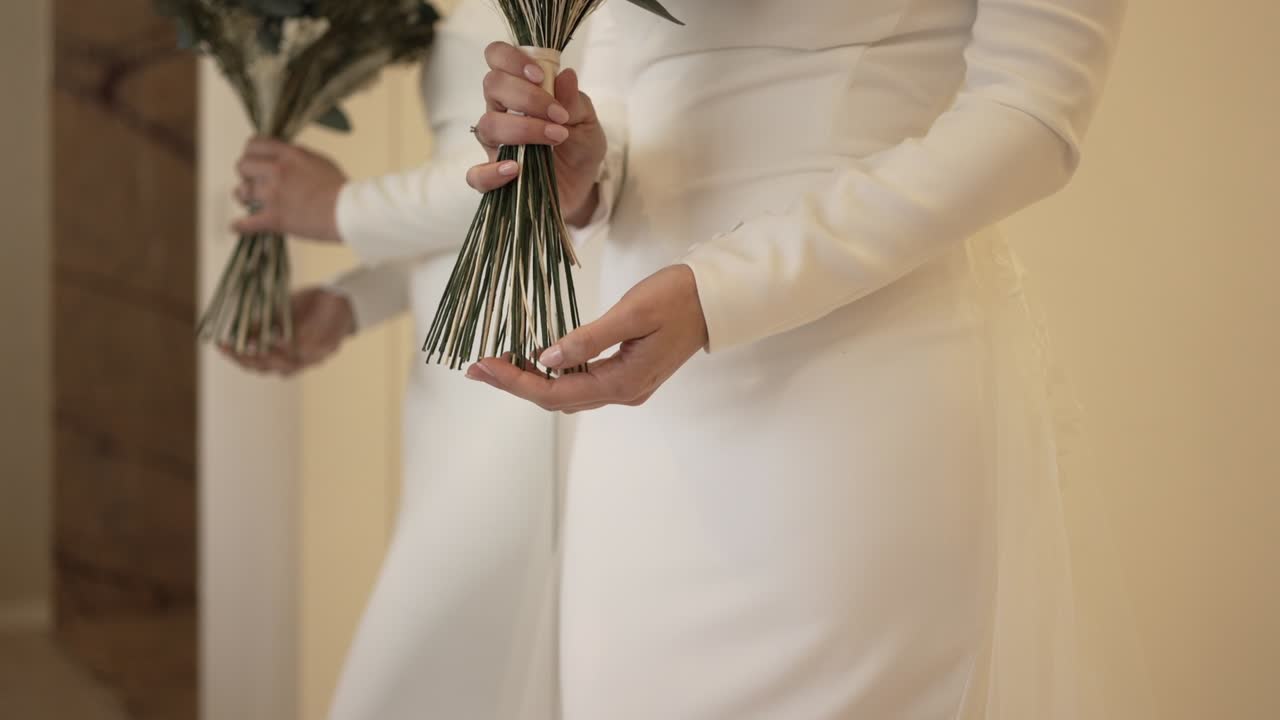 Bride in an elegant white gown holding a minimalist bouquet of long green stems, reflecting in a mirror