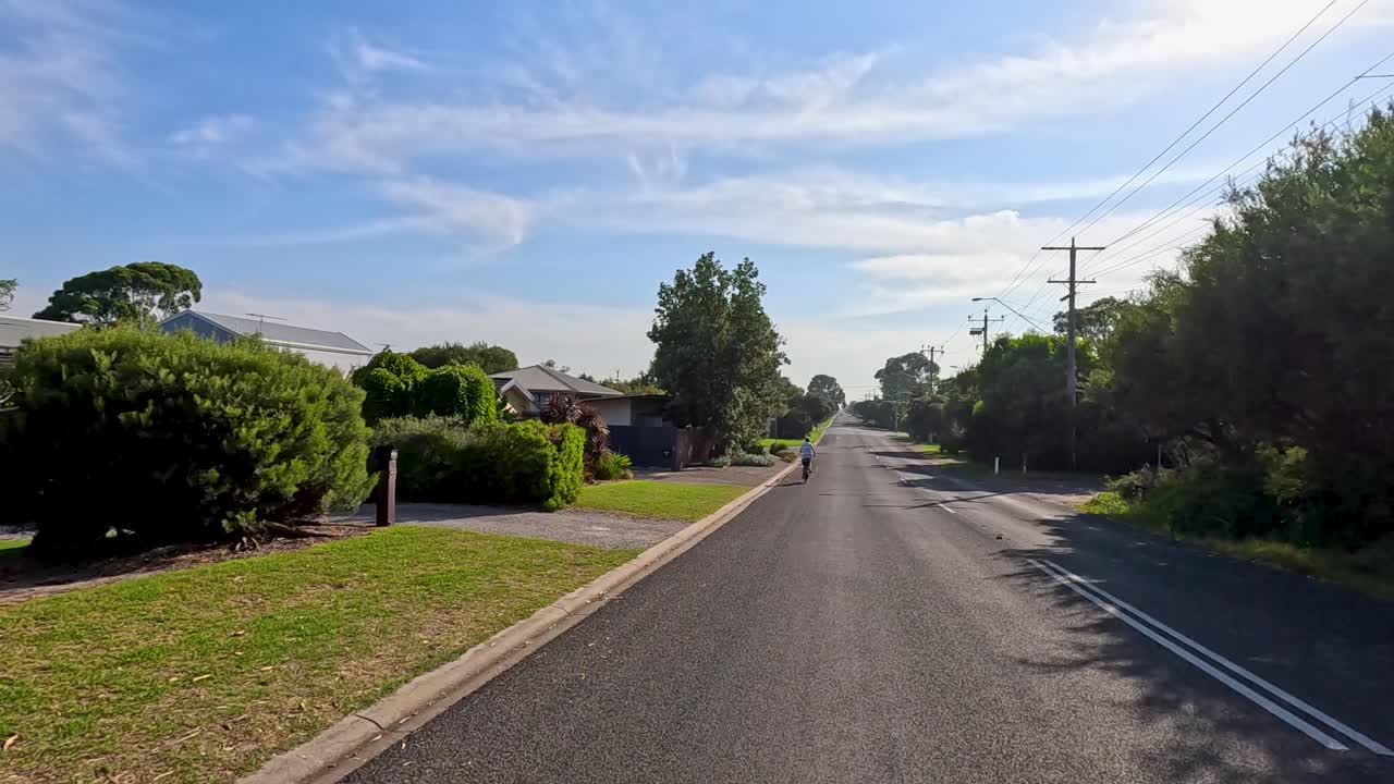 A cyclist rides through a quiet, sunlit residential street in Point Lonsdale, capturing serene suburban scenery