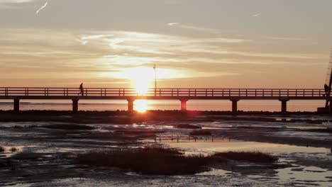 person walks on a small bridge in front of an old antique lighthouse while sunset