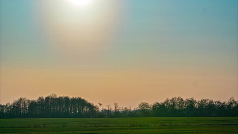 sun setting in time lapse as evening dawns, blue, lavender and orange colors over forested and grassland area