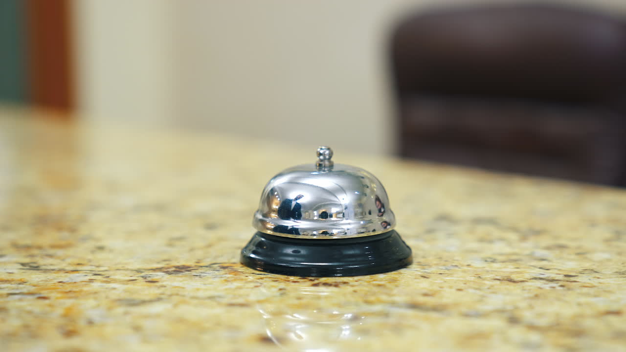 Metal bell button at hotel. Hand touching the electronic bell on the table to call a receptionist at a hotel. Close-up.