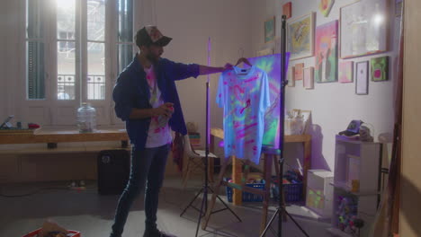 male designer spraying glow paint on t-shirt in art studio