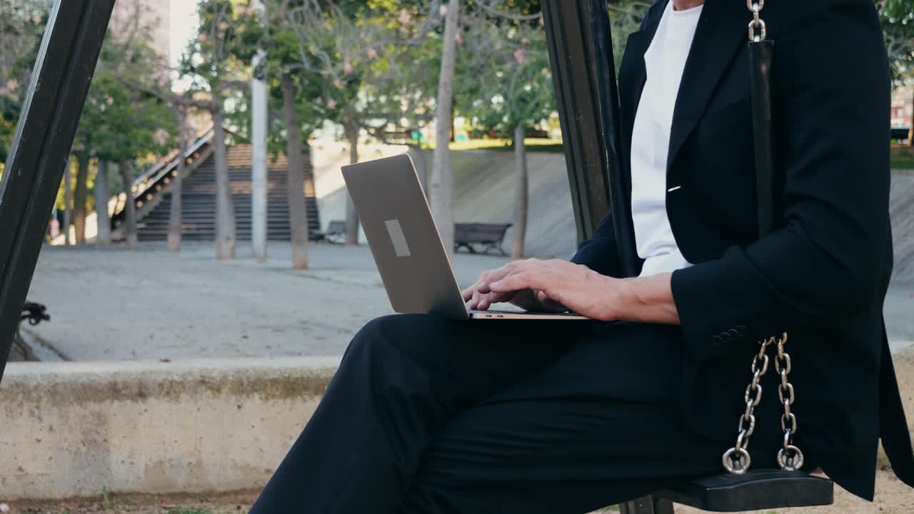 Businessman working on laptop in park swing