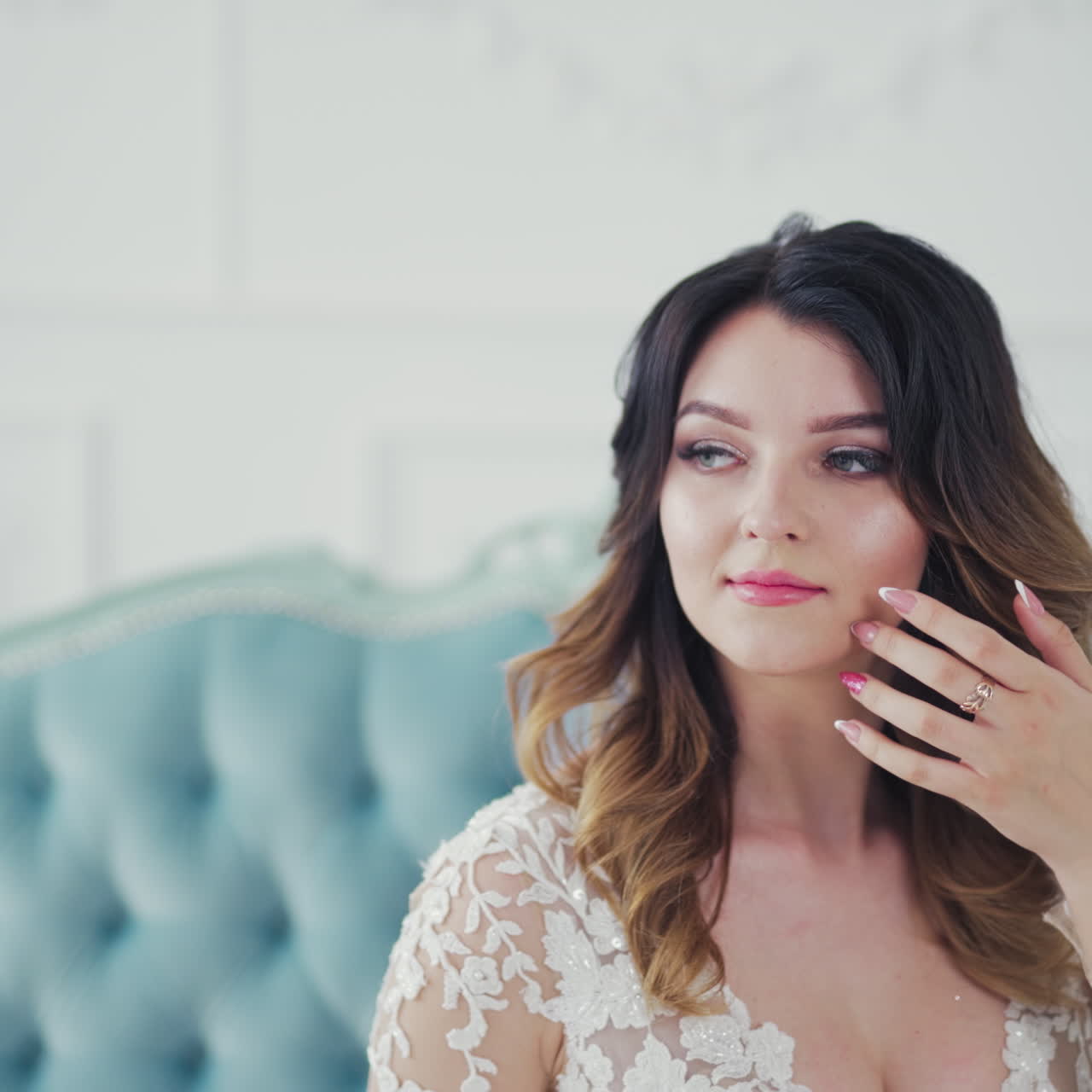 Stylish young bride sits on a couch and holds a beautiful tender flowers. Young model in white wedding dress is sitting in the light room.