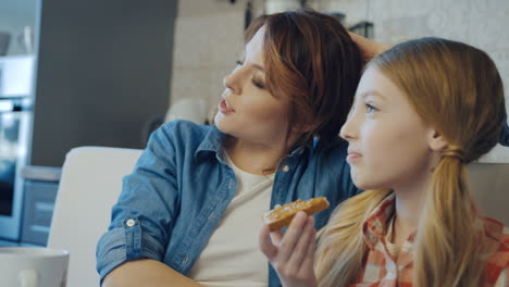 retrato de la mujer bonita y su hija adolescente rubia sentada, hablando y descansando mientras una niña come pan con mantequilla de maní. de cerca. en el interior