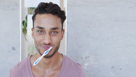 Portrait-of-happy-biracial-man-brushing-teeth-in-sunny-bathroom,-copy-space,-slow-motion