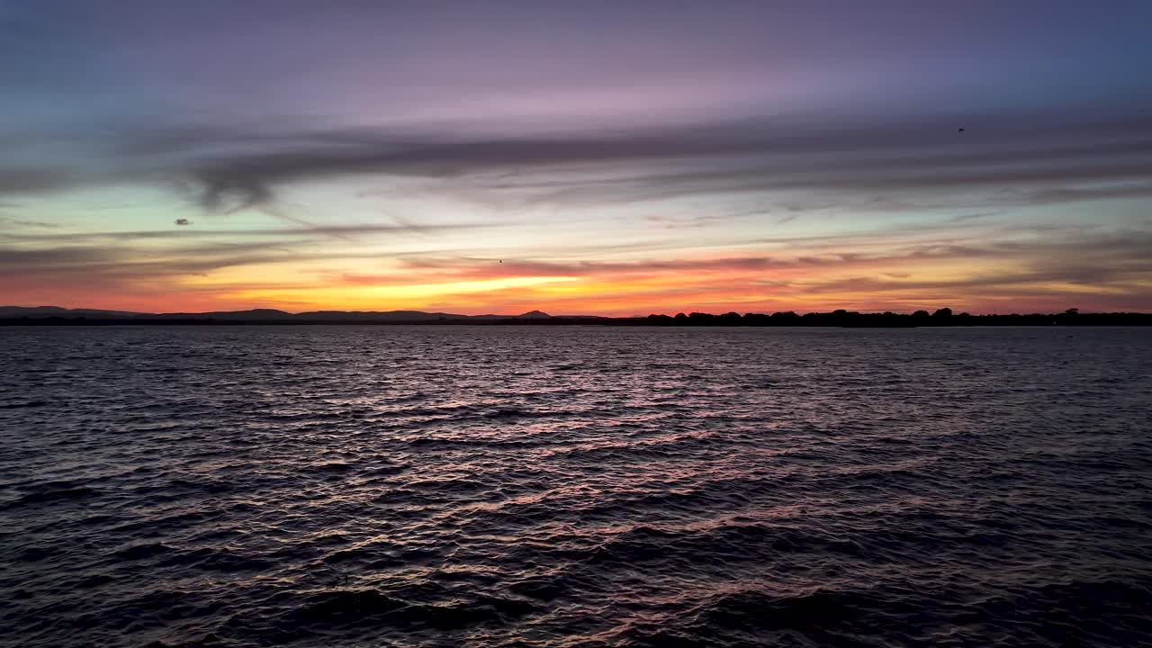 The setting sun is casting an orange glow on the water, creating a beautiful and dramatic scene
