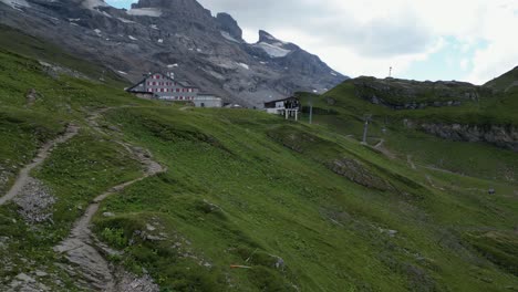 Push-in-drone-aerial-view-:-Mountain-Gravel-path-next-to-meadows-and-Rocky-mountain-peaks