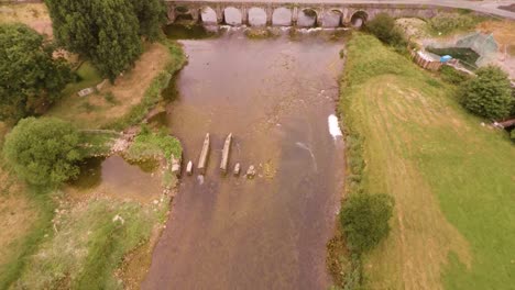 Flying-over-a-beautiful-flowing-lake-that-leads-to-an-old-brick-bridge