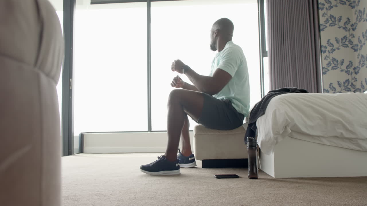 Sitting on bed, man relaxing in bedroom with water bottle and smartphone nearby