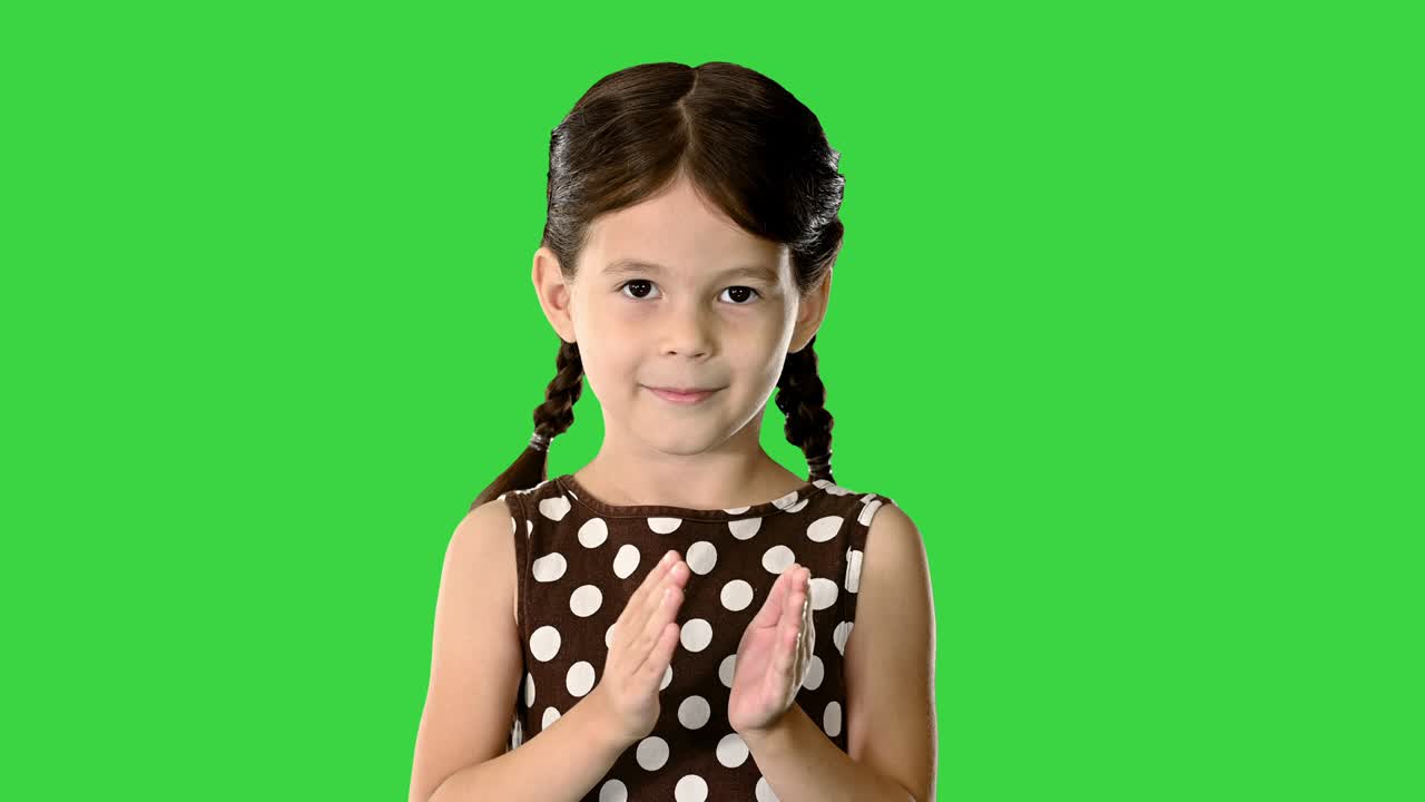 niña con vestido de puntos polca aplaudiendo sus manos mirando a la cámara en una pantalla verde, llave de croma