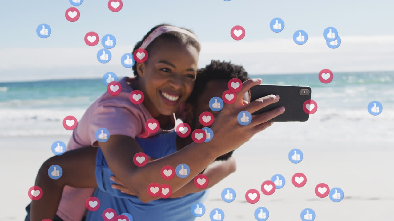 Animace ikon sociálních médií nad šťastným afroamerickým párem s chytrým telefonem na pláži.