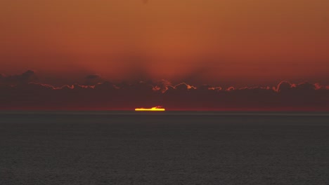 Sunset-timelapse-over-ocean-or-sea,-moving-orange-clouds,-sun-behind-horizon