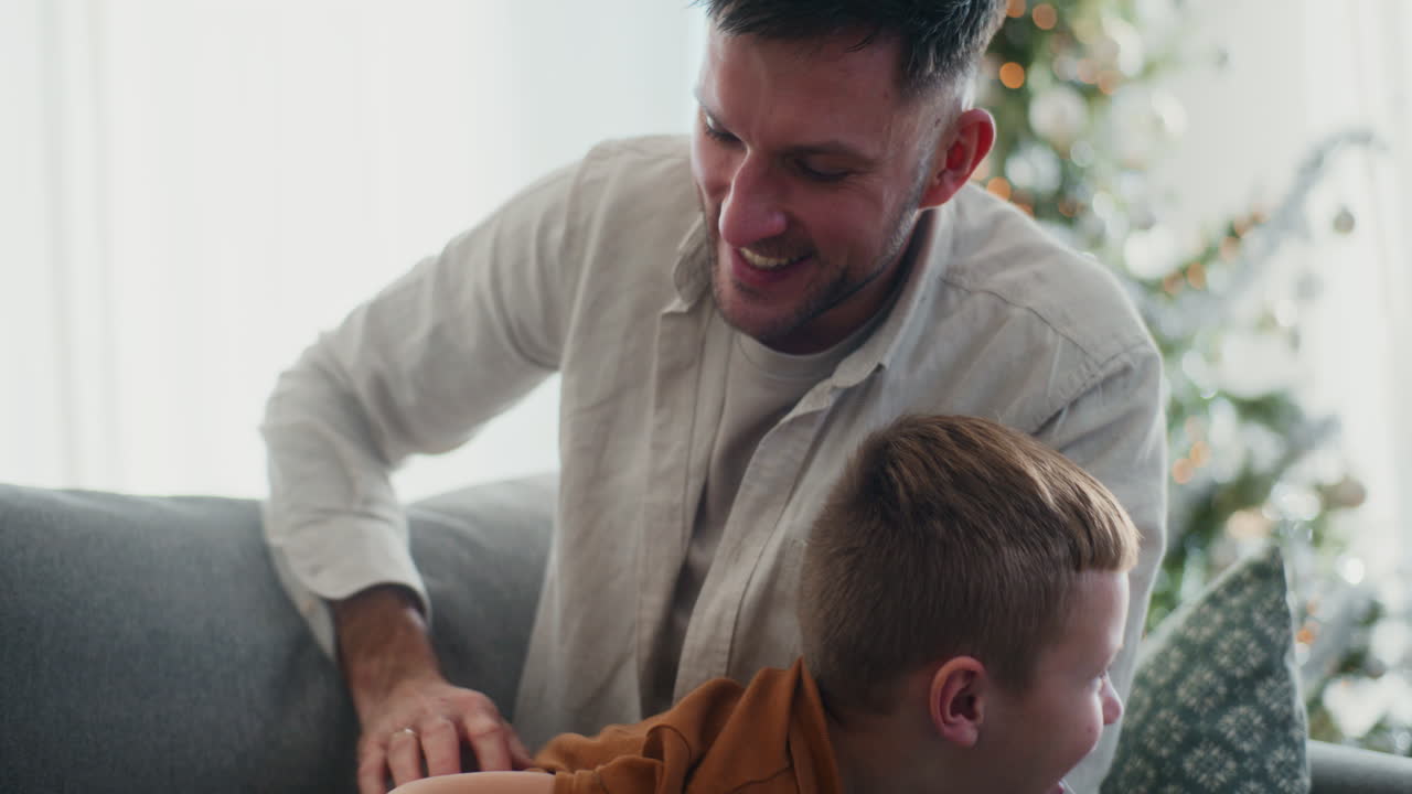 el padre abraza al hijo lo cosquillea y se regocijan en el sofá