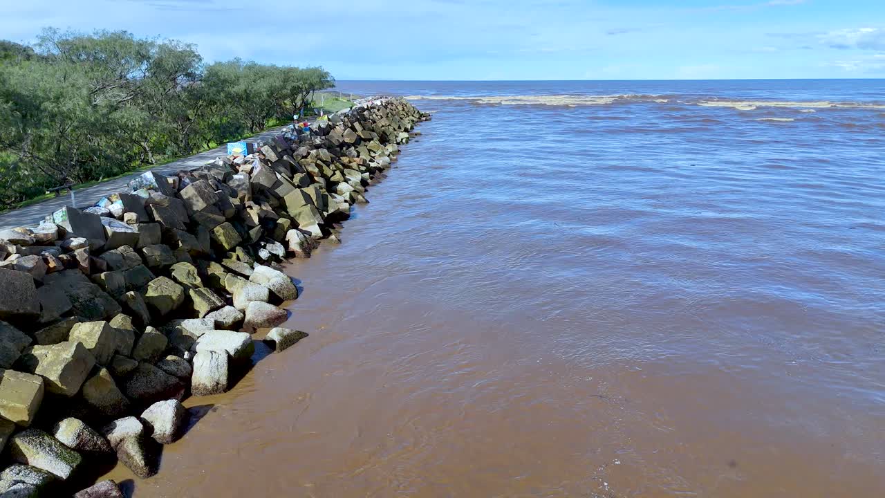Aerial drone view over stone breakwater at river mouth, calm water, lush green riverbank