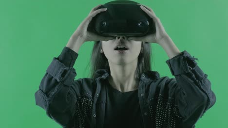 una mujer joven se pone un auricular de realidad virtual. casco de realidad virtual sobre el fondo verde. clave de croma