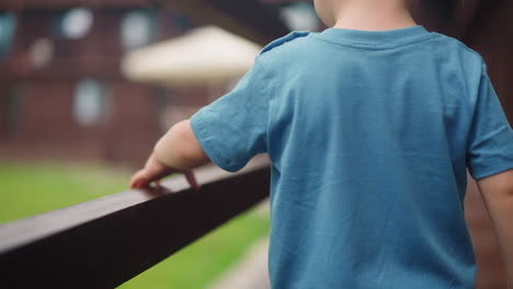 little child touches wooden handrail playing on veranda