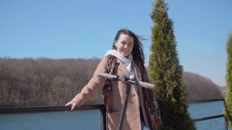 a young student girl with an electric scooter stands on the observation deck by the river. the girl breathes in fresh air and looks at the camera. modern gadgets for young people and business people