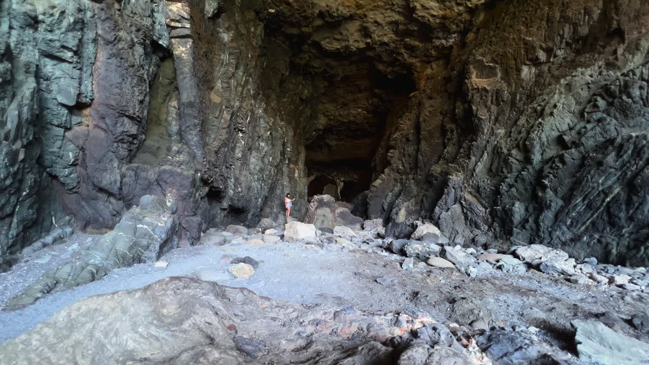 Entrance to the massive Ajuy sea caves in Fuerteventura, with people standing at the mouth showing the scale of the dark, imposing natural wonder. Canary Islands, Spain