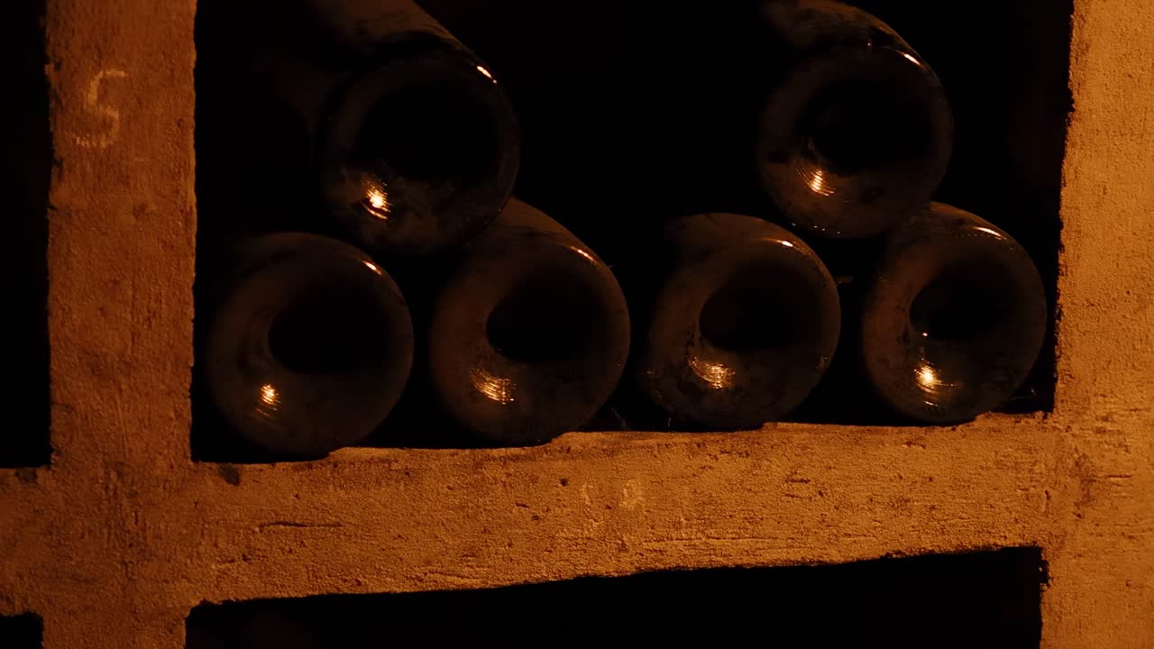 A close-up view of wine bottles stored horizontally on rustic shelves in a dimly lit environment.