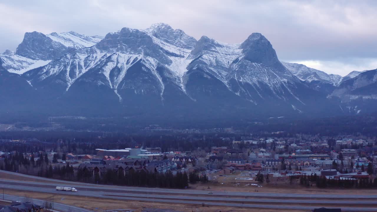 camión de 18 ruedas y autos recorren la autopista en primer plano con la cordillera de las tres hermanas en canmore alberta en canadá, disparo dinámico de drones