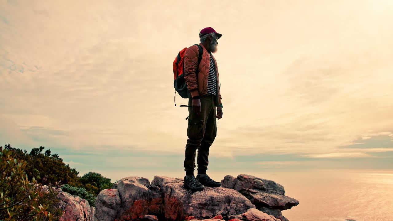 Man standing on rocky terrain with backpack enjoying ocean view