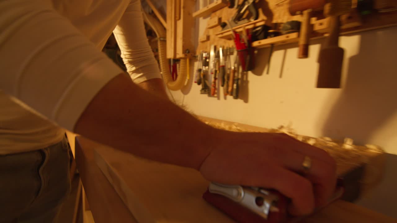 primer plano de una mano de hombre archivando una tabla de madera hecha por él en un taller casero