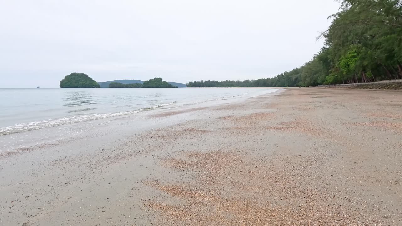 태국 크라비에 있는 노파라트 타라 해변의 조용한 풍경, 부드러운 빛 아래 평온한 물과 울창한 초록색을 보여줍니다.