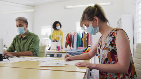 Female-fashion-designer-wearing-face-mask-sketching-clothing-design-at-studio