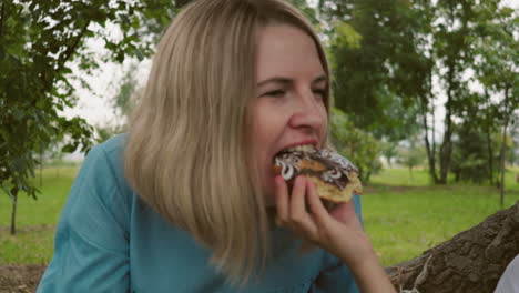 a close-up of a woman taking a bite of a chocolate-covered cake, with a hand offering it to her