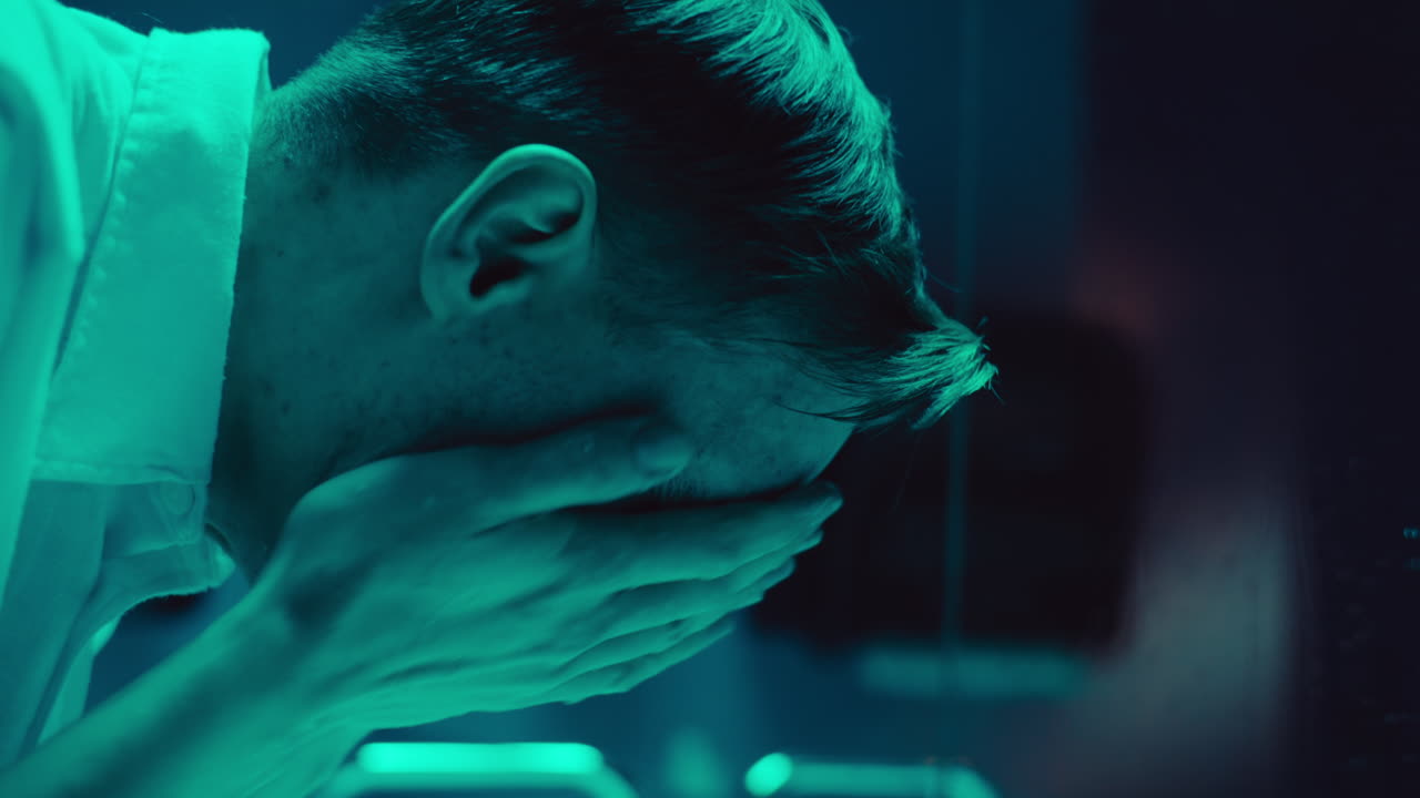 Uomo che si lava il viso in un bagno illuminato di verde acqua