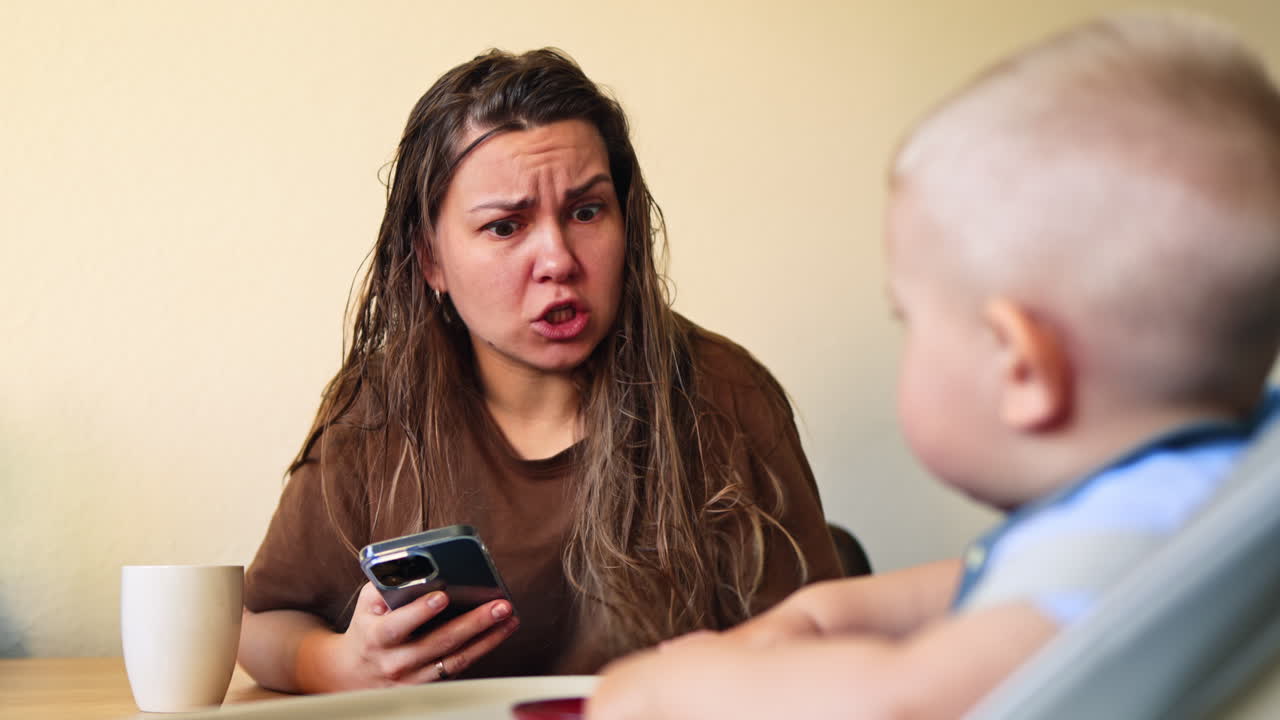 Mom with phone in hands yelling at her little child. Tired woman from motherhood yelling at her 1 year old son. Postpartum depression in woman