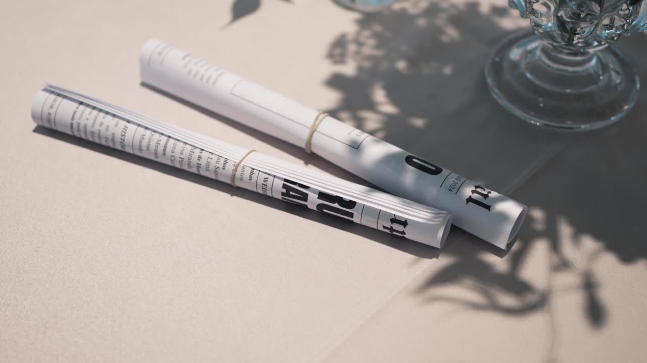 rollos de periódicos con bandas de goma en una mesa, proyectando una sombra