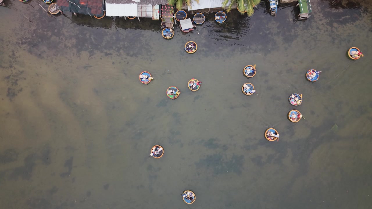 Mensen peddelen in ronde geweven mandboten in ondiep water nabij de kust in Hoi An, Vietnam, vastgelegd vanuit een hoog luchtdroneperspectief