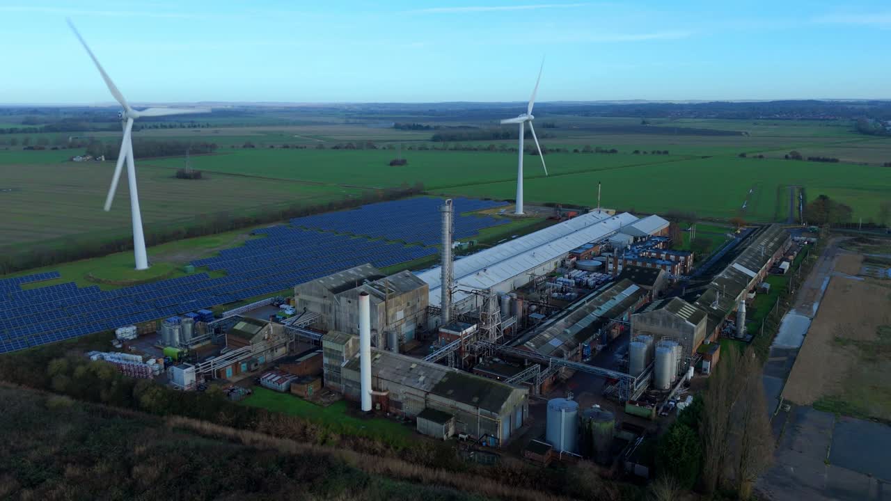 Corporate renewable energy aerial overview of a King's Lynn factory featuring integrated wind turbines and solar arrays for industrial power