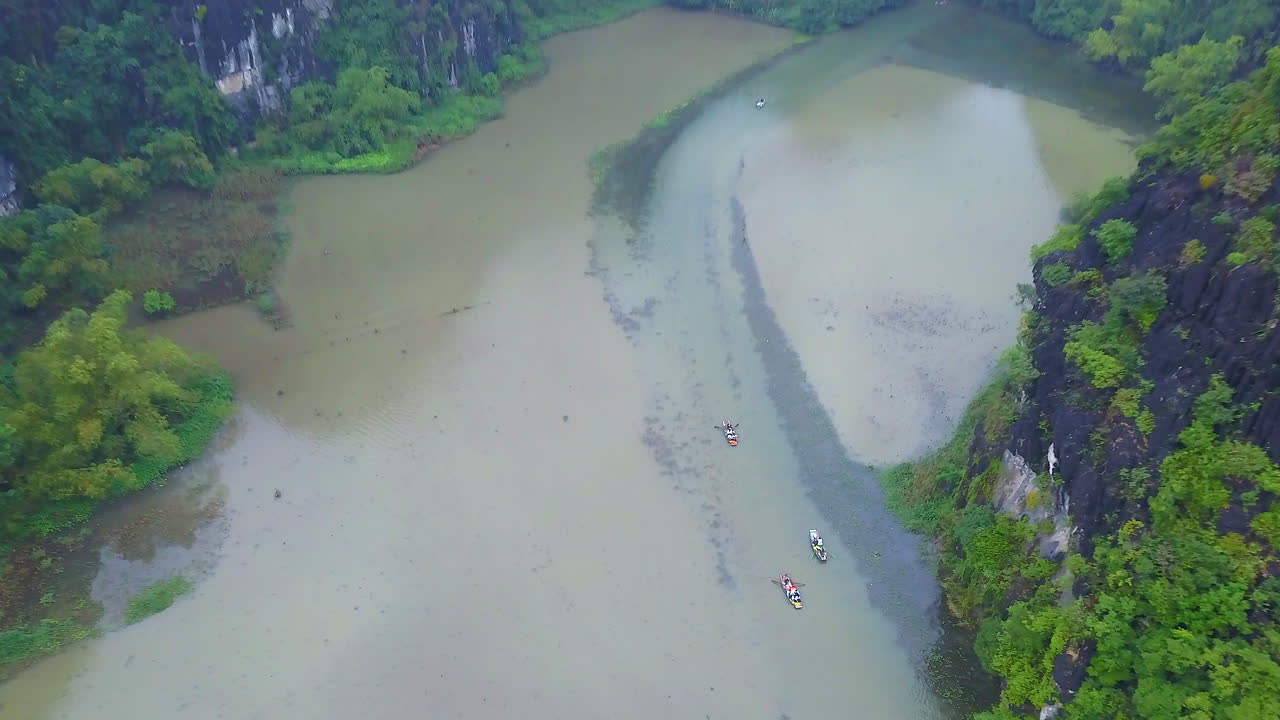 Cinematic drone footage of majestic limestone peaks in misty and foggy weather. Ricefields in wild jungle in the spring with boat tour canal in Tam Coc, Ninh Binh, Vietnam