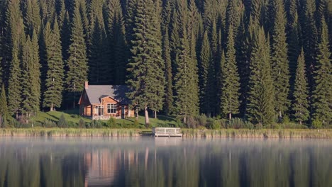 early morning mist floats over a serene lake reflecting a cozy lakeside cabin nestled among a dense pine forest, creating a tranquil and idyllic retreat