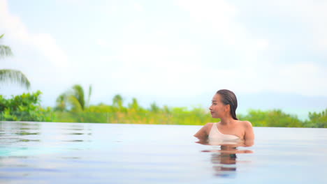 tropical island resort luxury destination with attractive asian lady relaxing in calm swimming pool overlooking the lush landscape and ocean in background