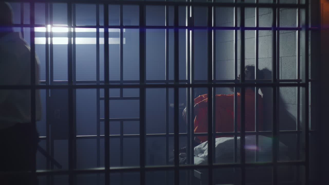 el prisionero se sienta en la cama en la celda de la prisión el carcelero camina por el pasillo