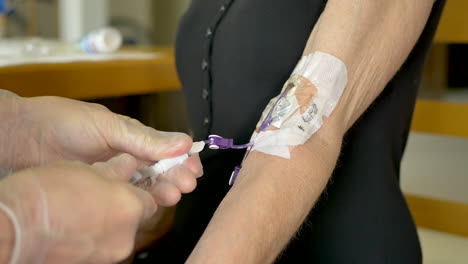 enfermera médica realizando una visita al paciente por vía intravenosa en casa usando guantes estériles mientras termina una inyección de solución salina con una jeringa en una línea picc y la tapa