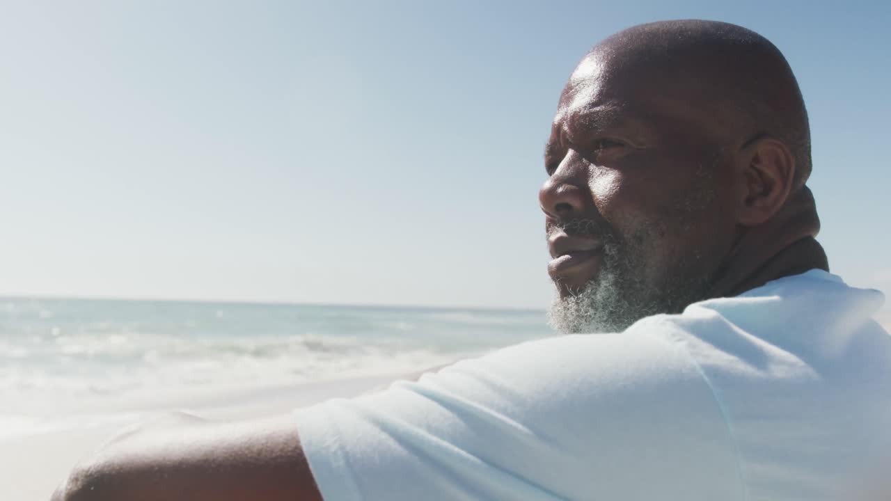Senior african american man wearing white tshirt sitting on sunny beach