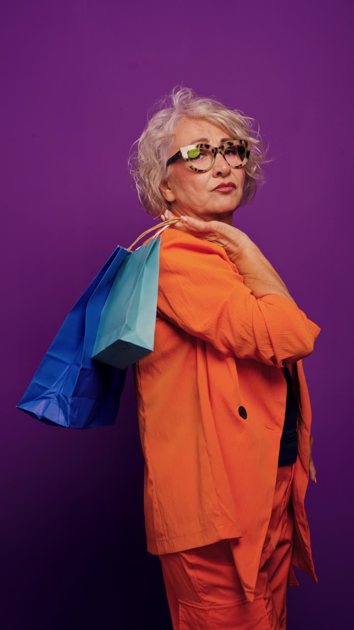 Elegante signora anziana in posa con borse della spesa su sfondo viola