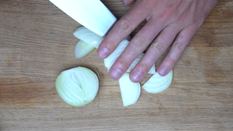 top down shot of a medium white onion being cut in slices with a chef knife