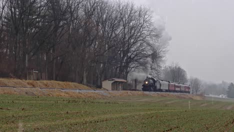 a steam engine and passenger cars traveling up grade in a lite snow storm