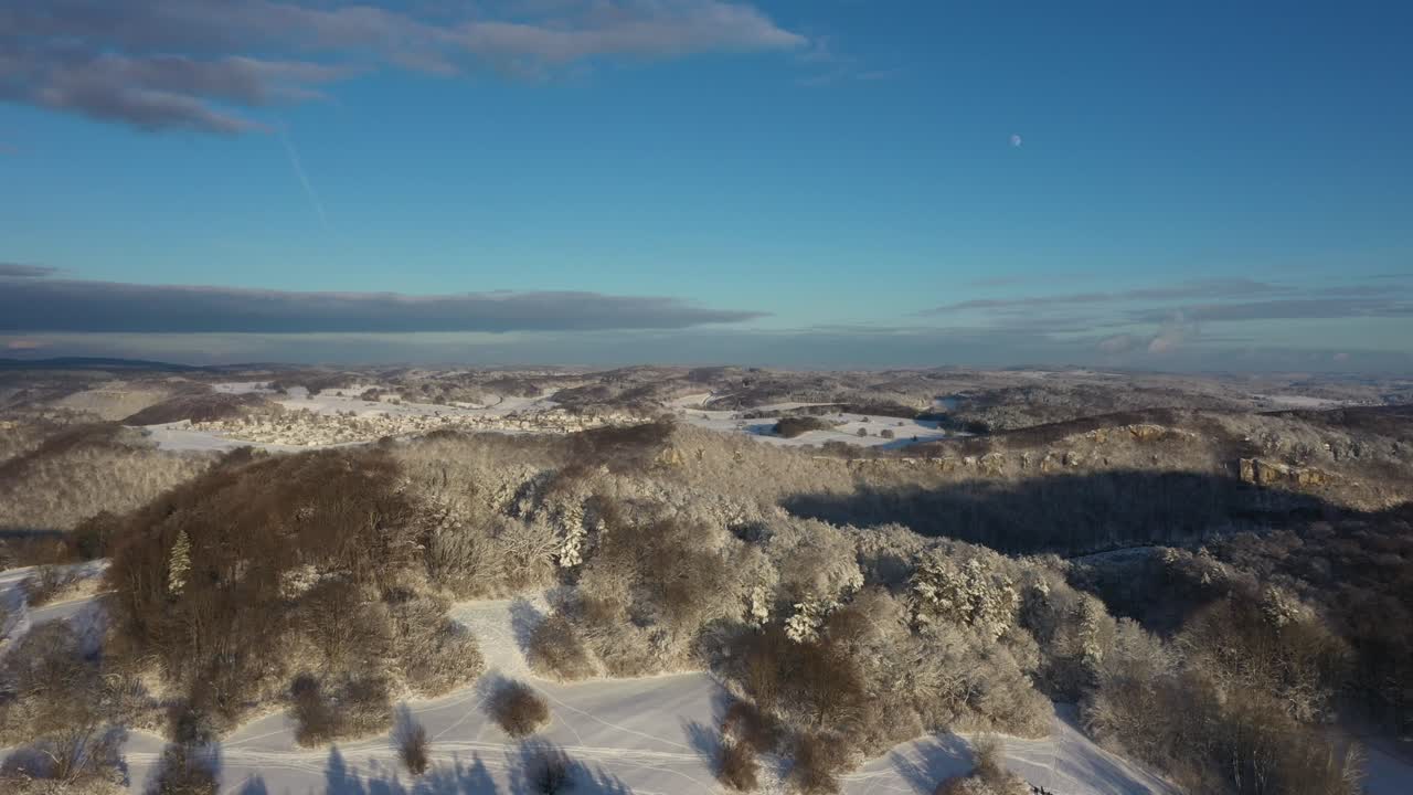 vuelo aéreo sobre montañas cubiertas de nieve y bosques con cielo azul durante el invierno en swabia, alemania